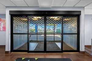 A hotel entrance with a glass door, a tiled floor, and a view of the parking area.