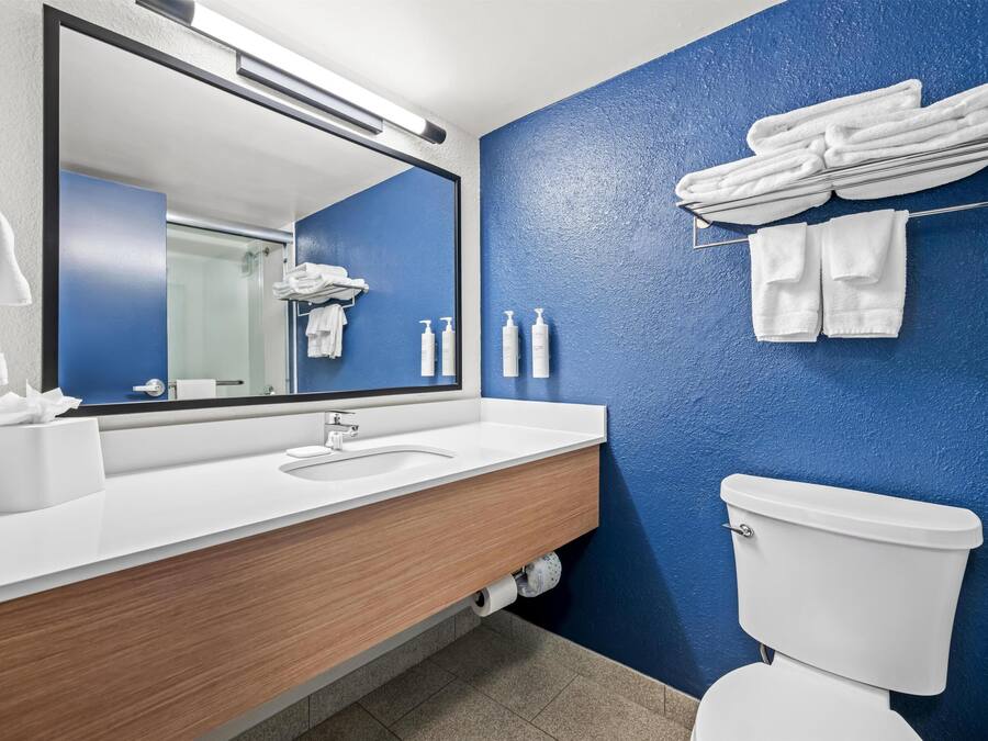 A modern bathroom with a blue accent wall, a wooden vanity, a white sink, a toilet, and a towel rack with folded towels.
