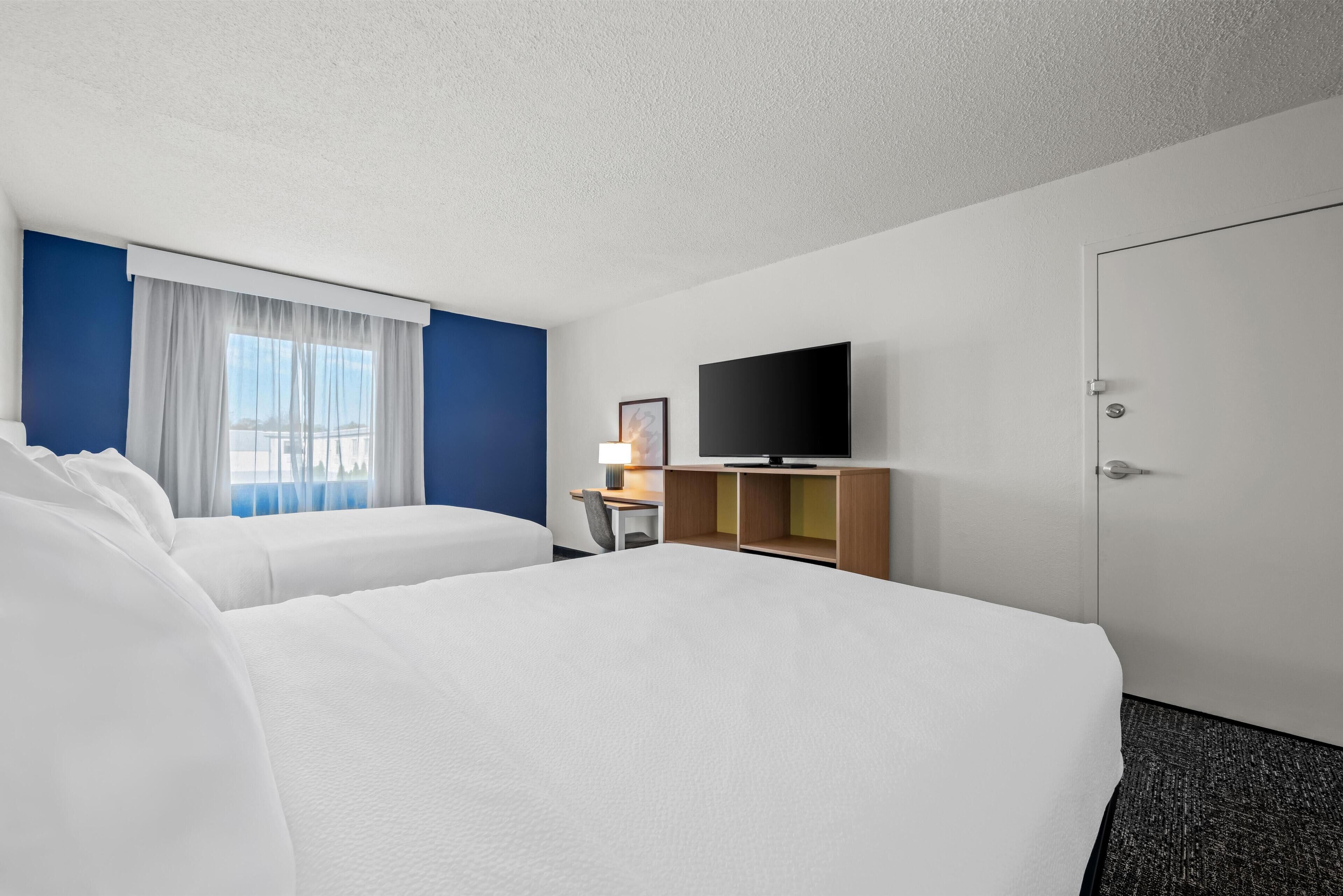 Une chambre d’hôtel avec deux lits, une télévision, un bureau et une fenêtre avec des rideaux.
