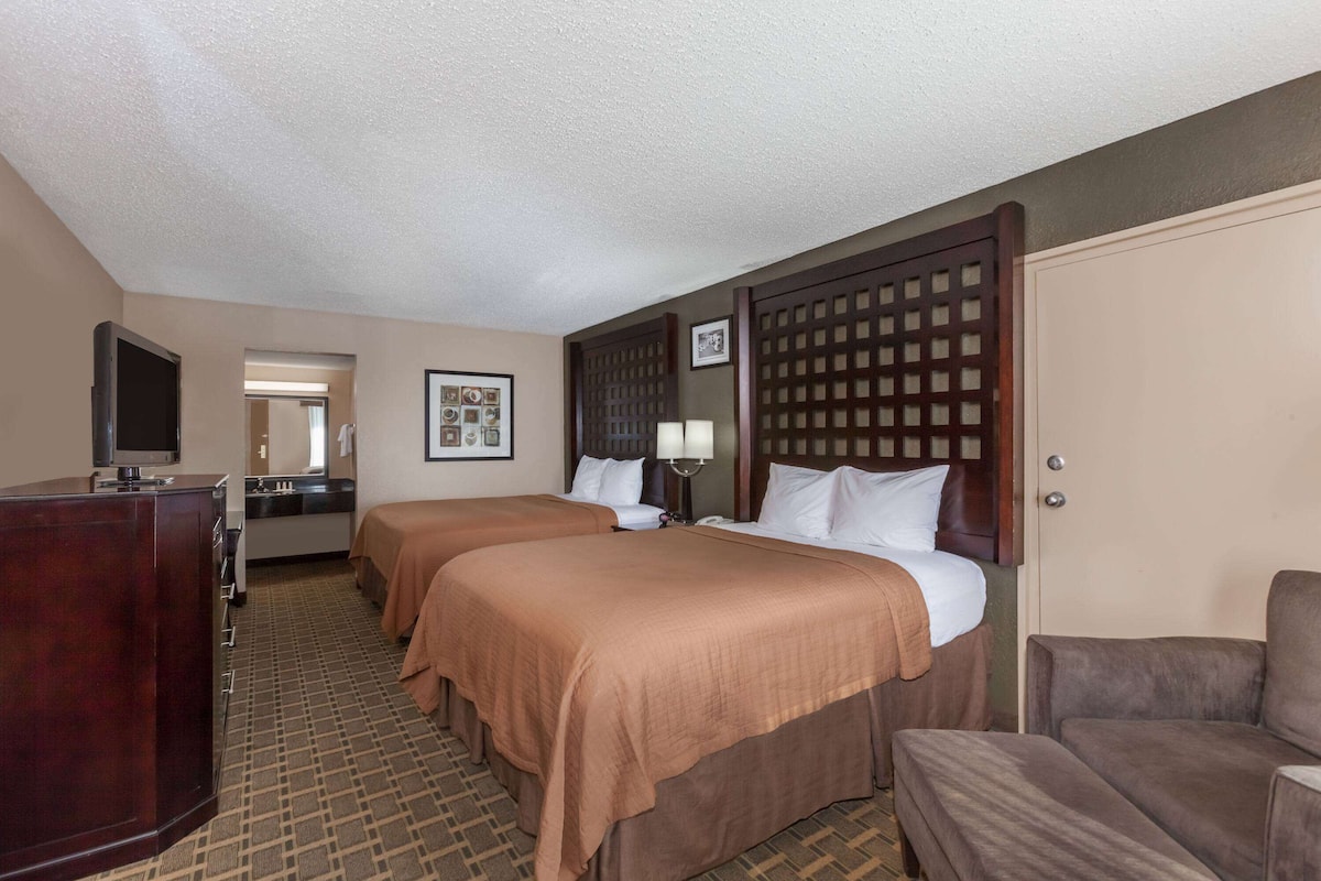 A hotel room with two beds, a desk, a TV, and a bathroom visible through an open door.