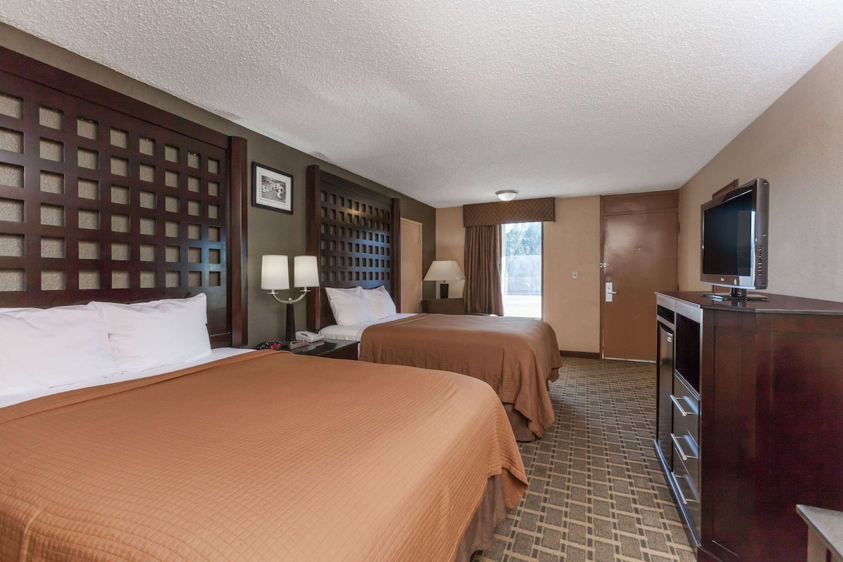 A hotel room with two beds, a TV, a desk, and a window with curtains.