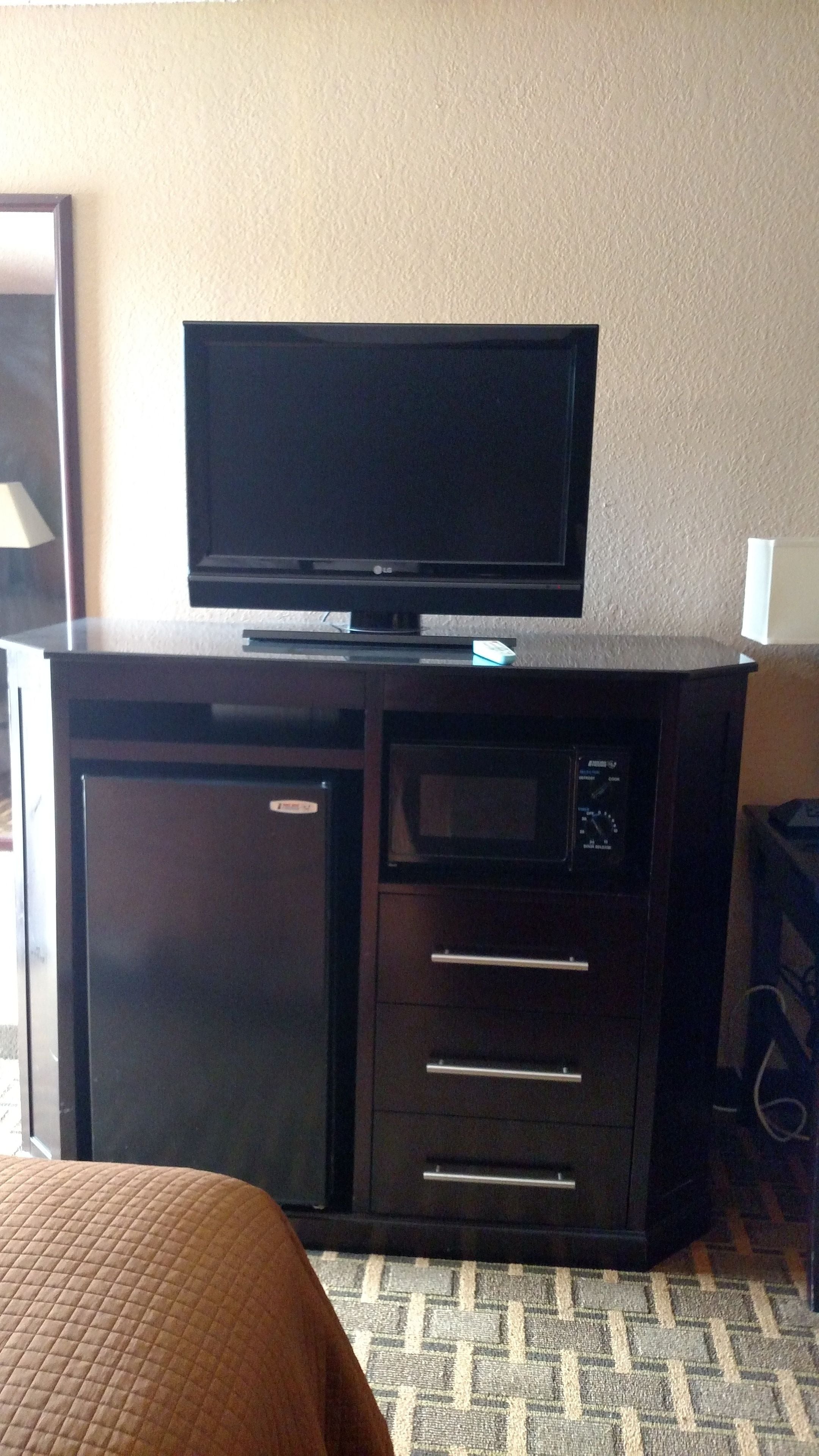 Habitación de hotel con televisión de pantalla plana en un mueble, microondas y un refrigerador pequeño.