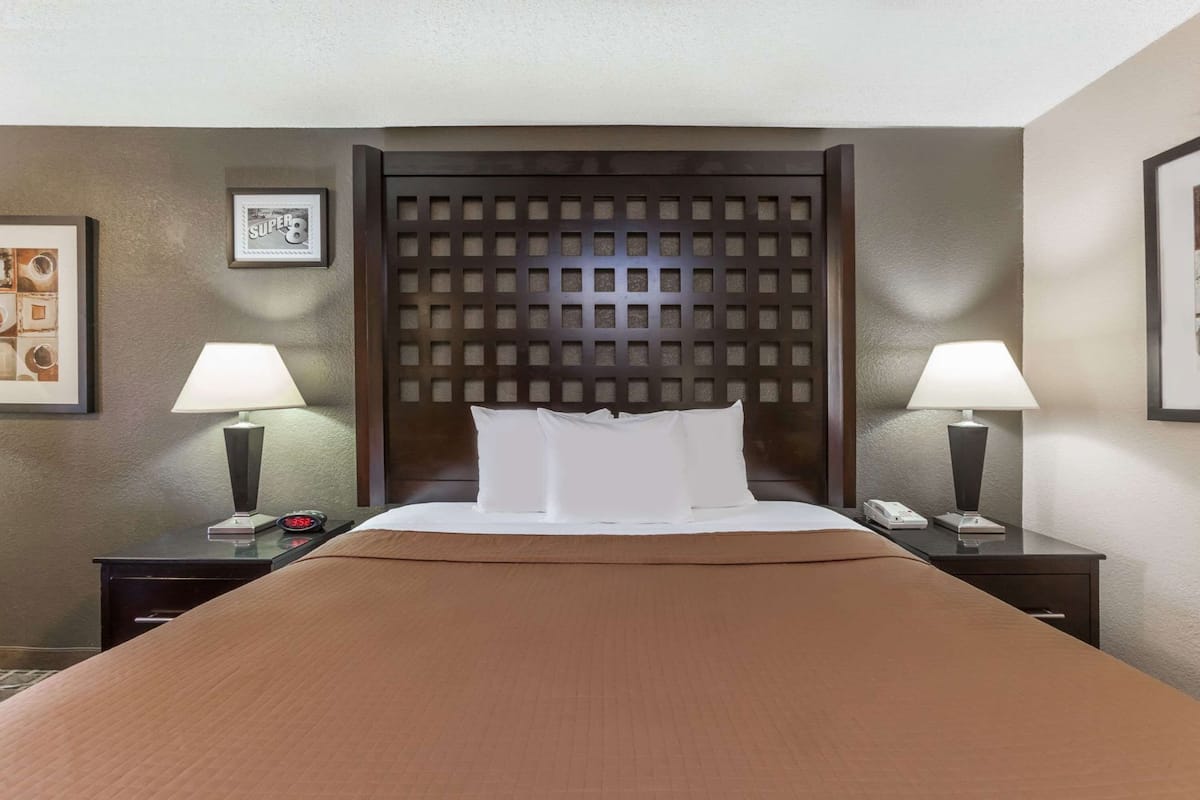 A hotel room with a large bed, two bedside tables with lamps, a clock, and framed pictures on the walls.