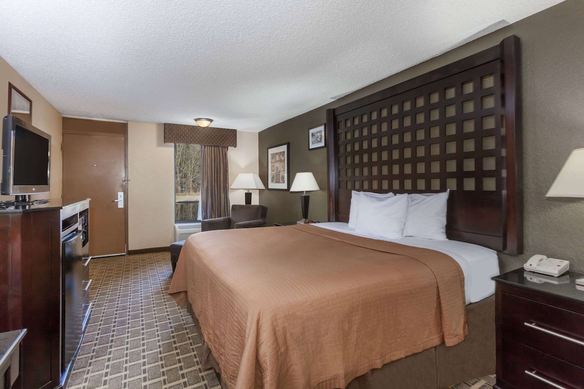 A hotel room with a large bed, a desk with a telephone, a television, and a window with curtains.