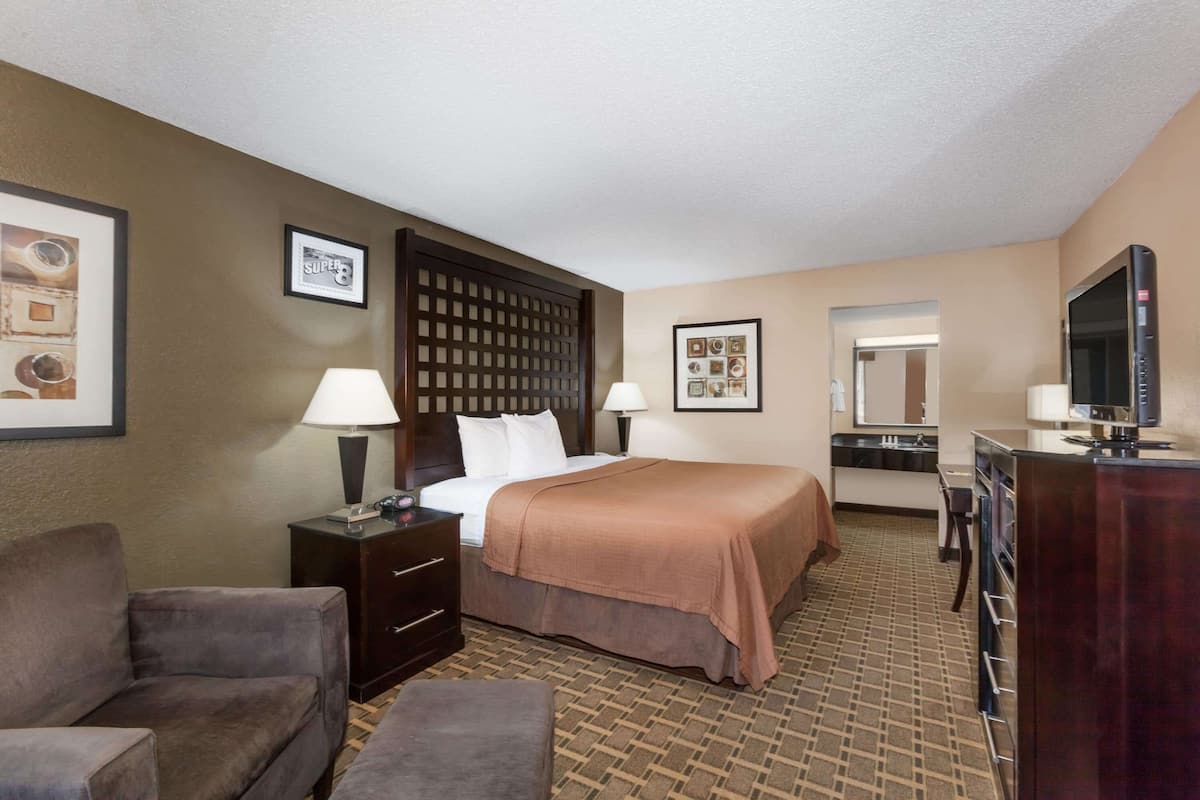 A hotel room with a bed, two bedside tables with lamps, a chair, a desk with a television, and a mirror.