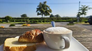 A white cup with a spoon, a slice of bread, and a croissant on a white plate.