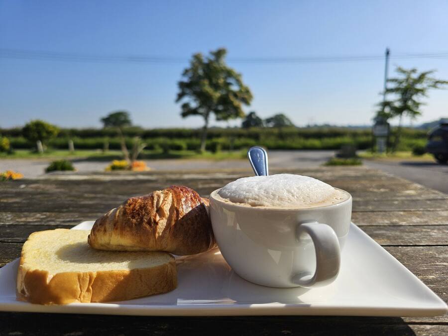 A white cup with a spoon, a slice of bread, and a croissant on a white plate.
