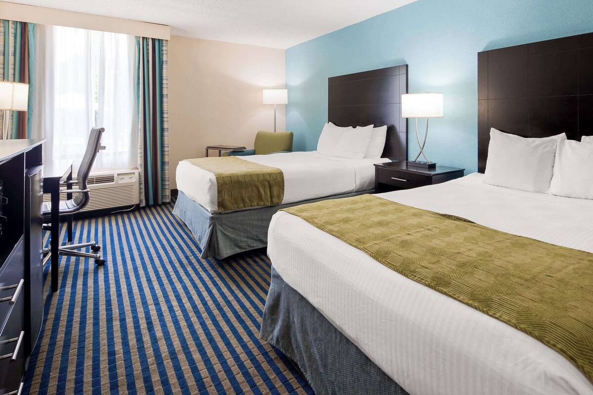 A hotel room with two beds, a desk, and a chair.