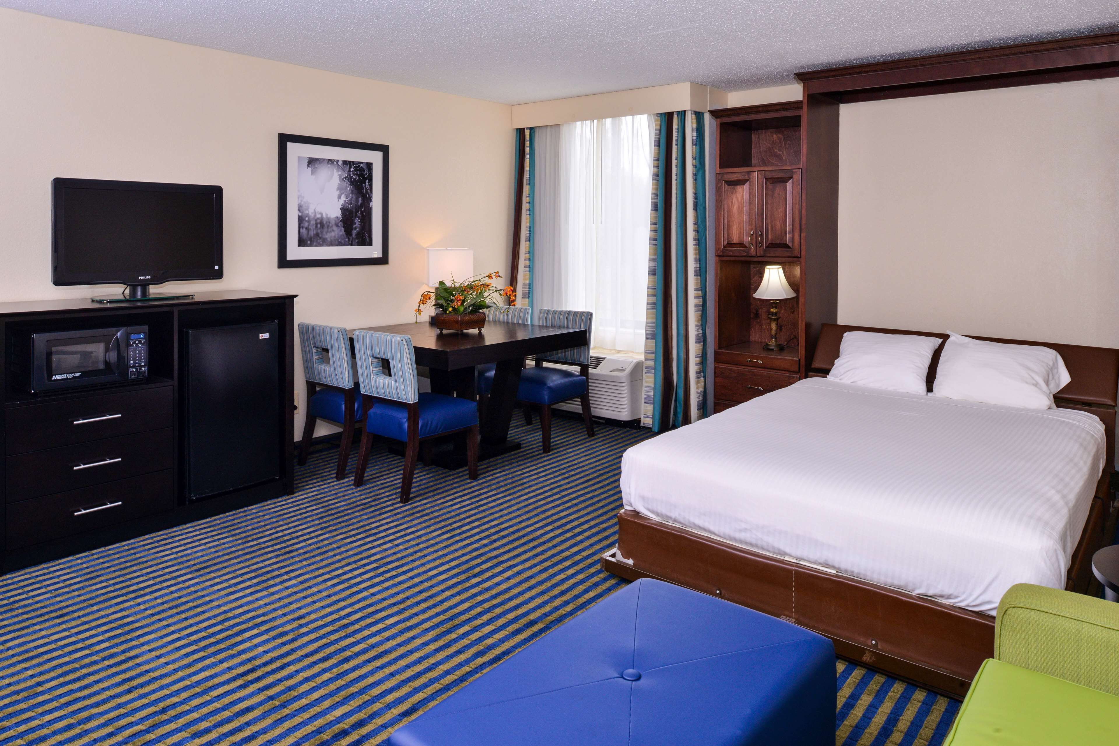 A hotel room with a bed, a desk with a chair, a television, a microwave, and a cabinet.