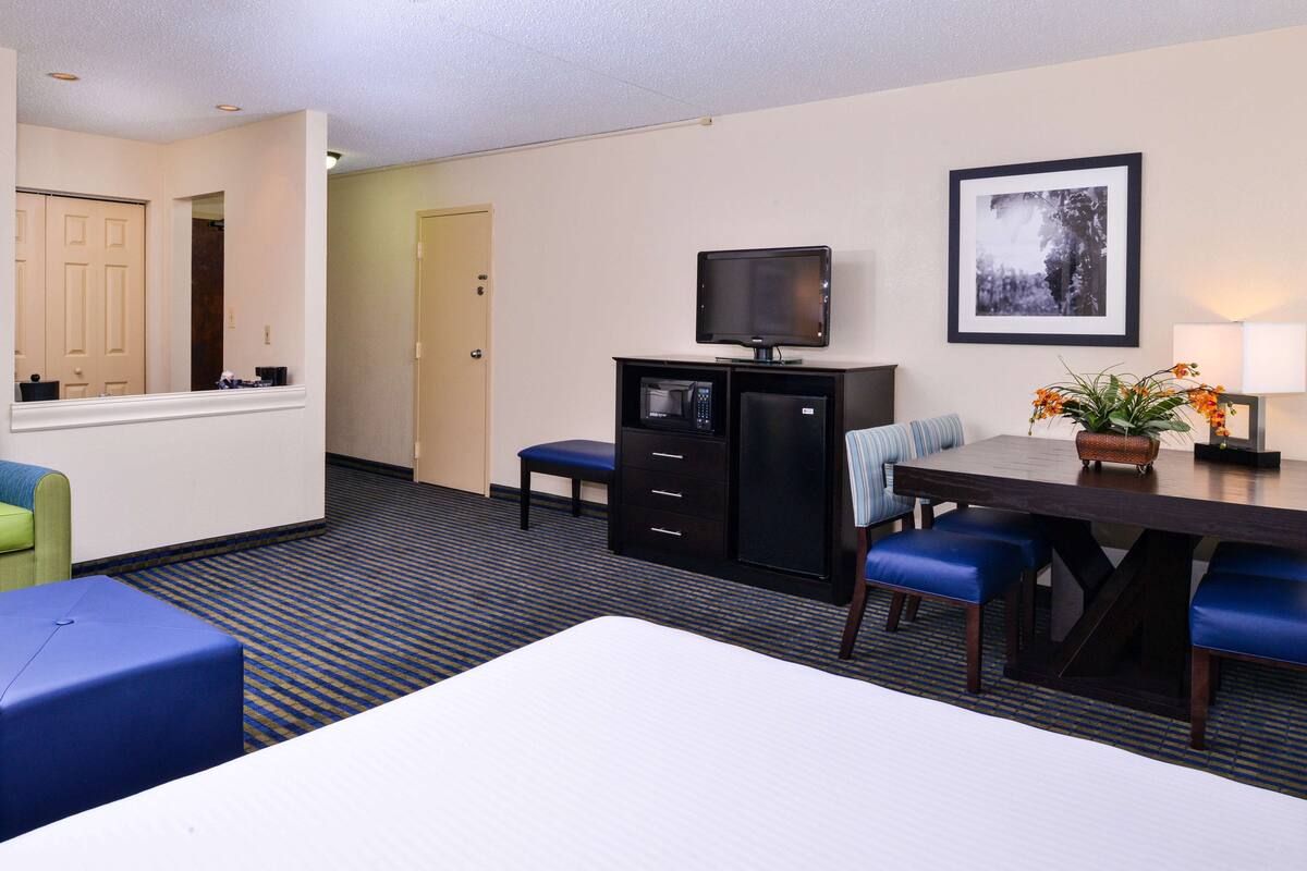 A hotel room with a bed, a desk with a computer, a television, and a dining table with chairs.