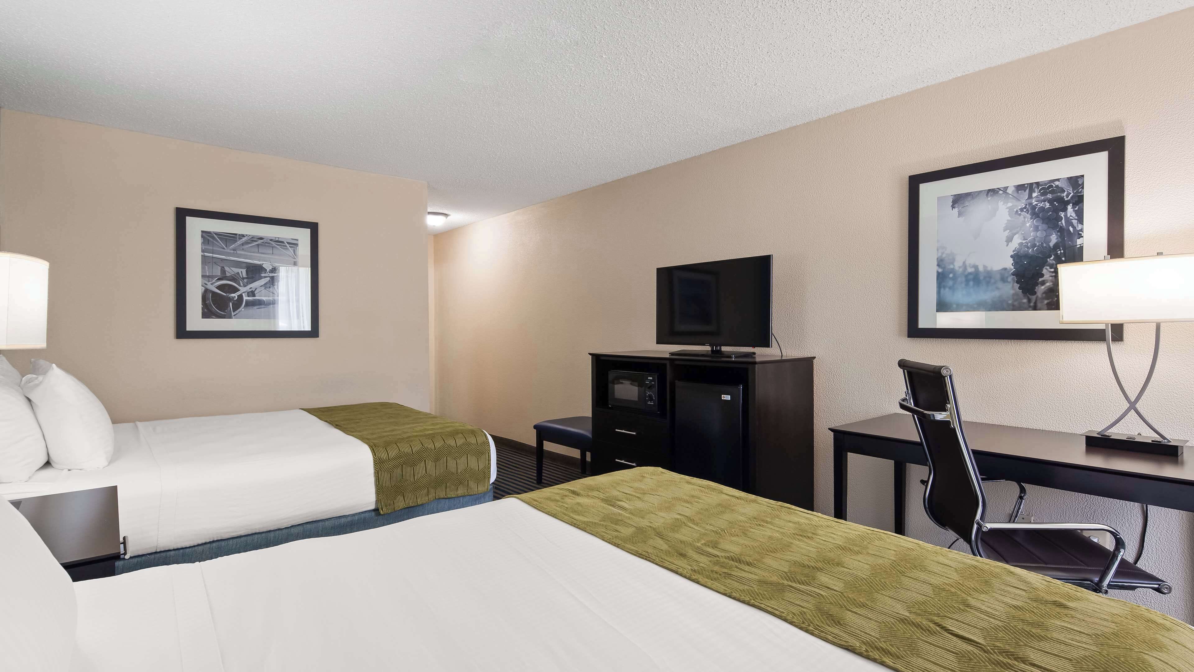A hotel room with two beds, a desk with a television, a chair, and two framed pictures on the wall.