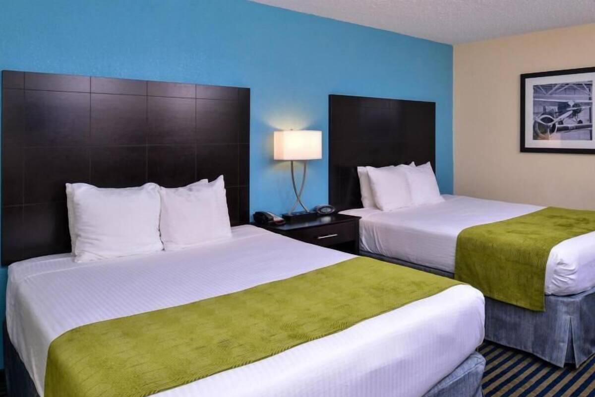 A hotel room with two beds, a nightstand with a lamp, and a framed picture on the wall.