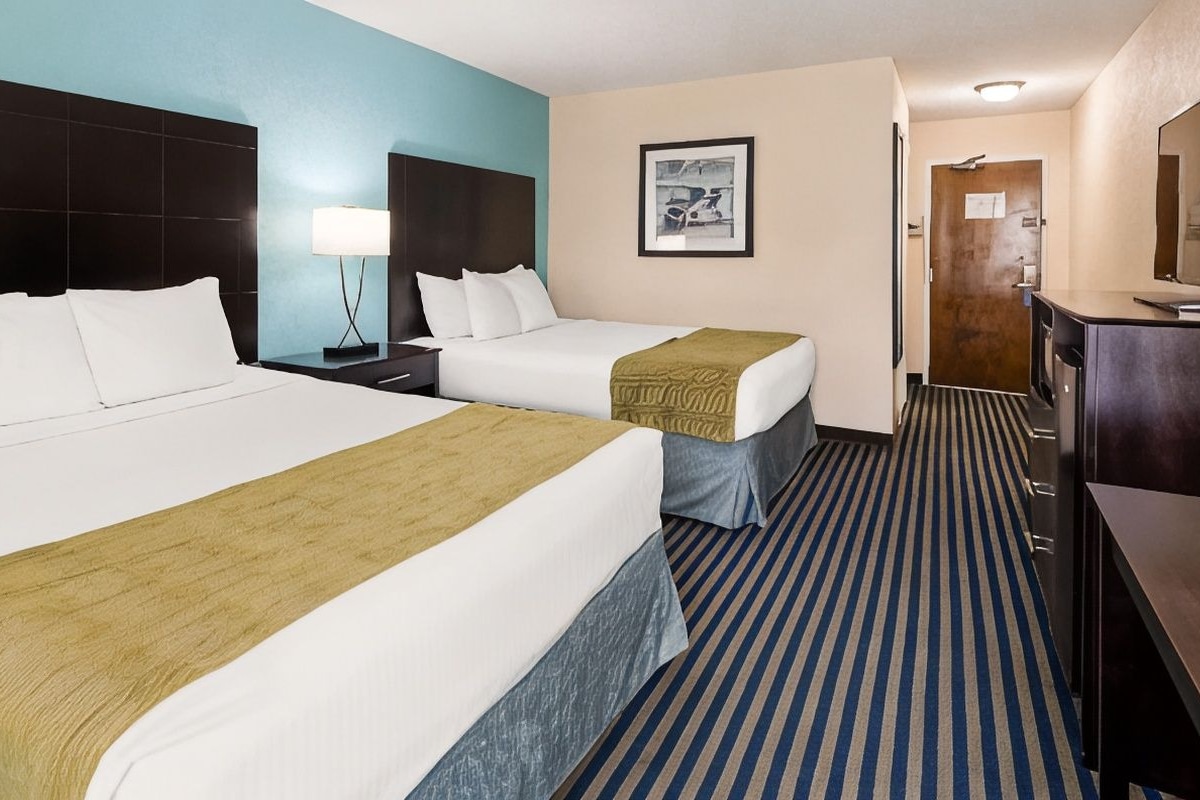 A hotel room with two beds, a desk, a chair, a lamp, a picture on the wall, and a door.
