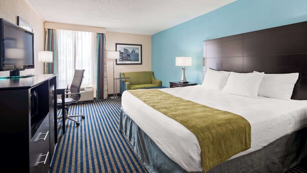 A hotel room with a large bed, a desk with a TV, a chair, a desk lamp, and a window with curtains. - Best Western Leesburg Hotel & Conference Center (Leesburg)