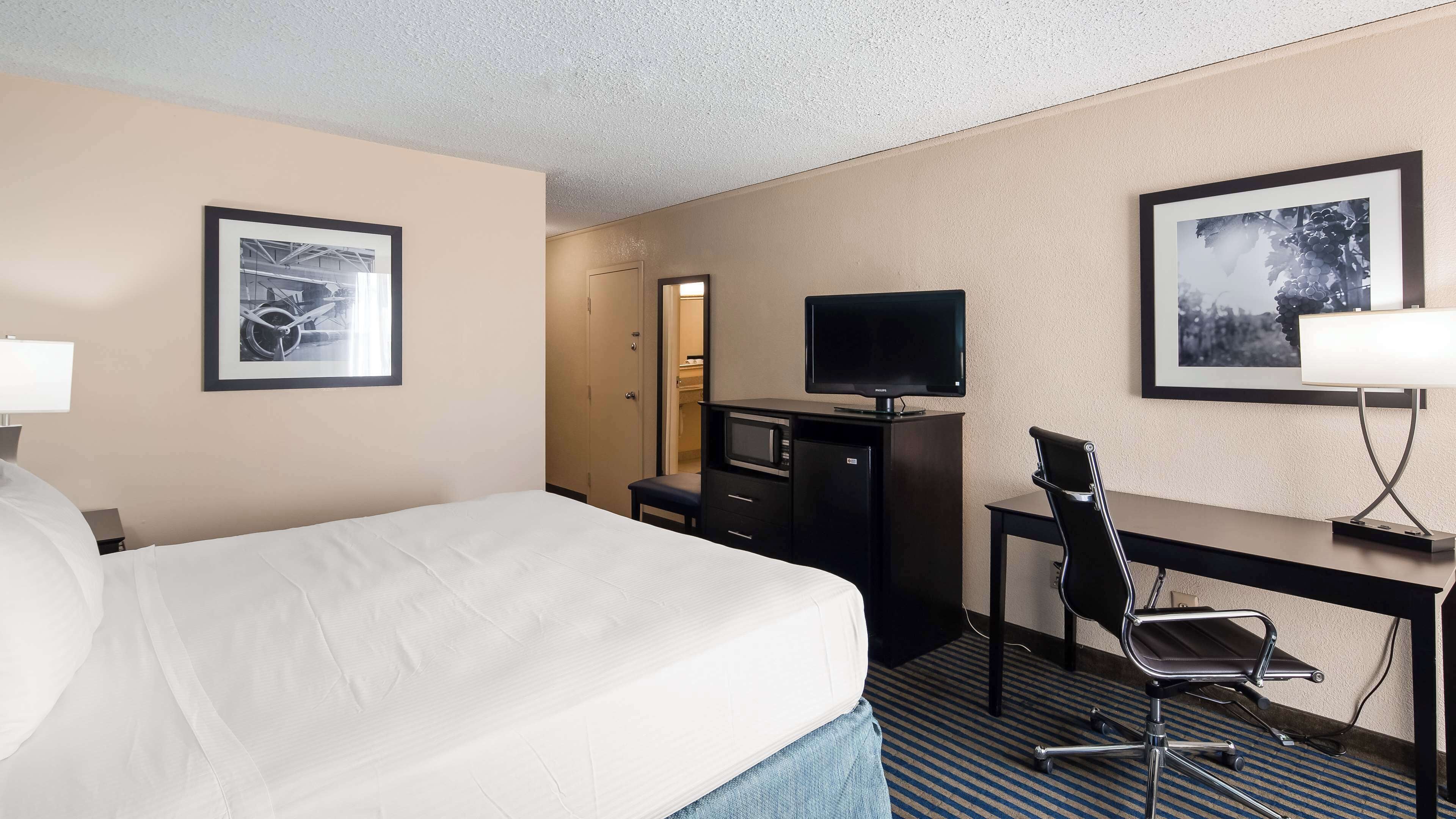 Una habitación de hotel con una cama, un escritorio y una silla, televisión y cuadros en las paredes.