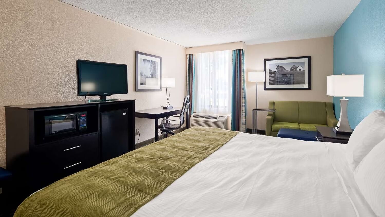 A hotel room with a bed, a desk, a television, a microwave, a chair, and a lamp.