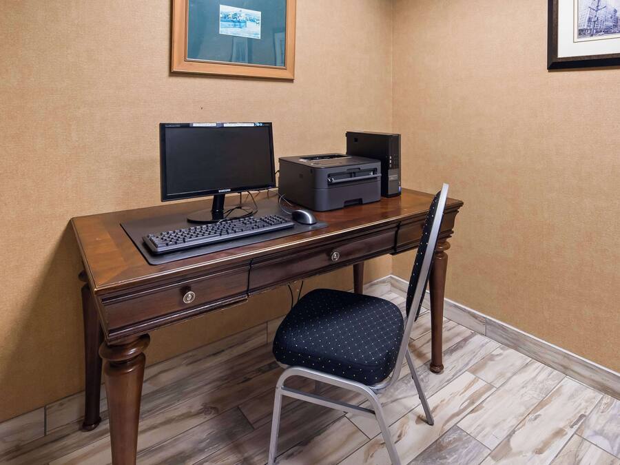 A wooden desk with a computer, monitor, and printer. A chair is positioned in front of the desk.
