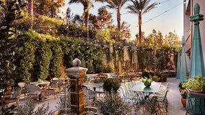 An outdoor patio area with tables and chairs, a central fountain, and lush greenery.