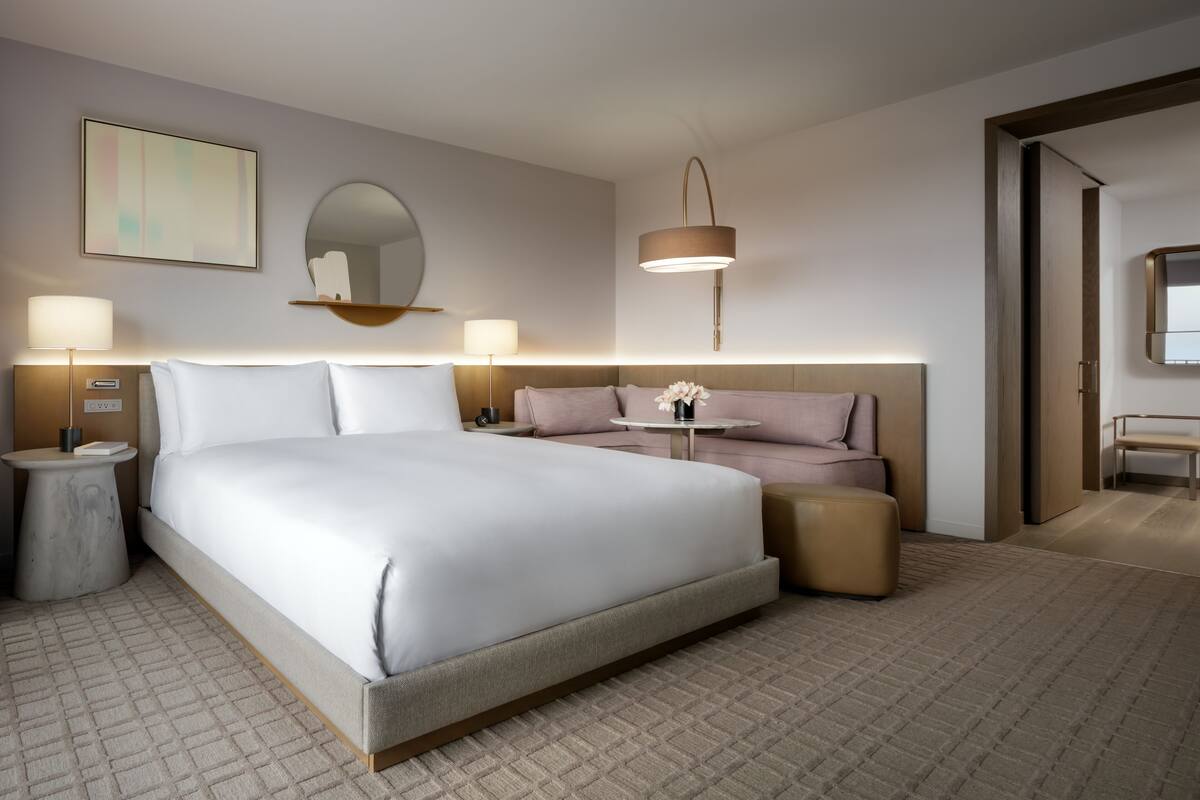 Ein modernes Hotelzimmer mit einem großen Bett, Nachttischen, einem Spiegel, einer Wandlampe und einem kleinen Tisch mit Blumen.