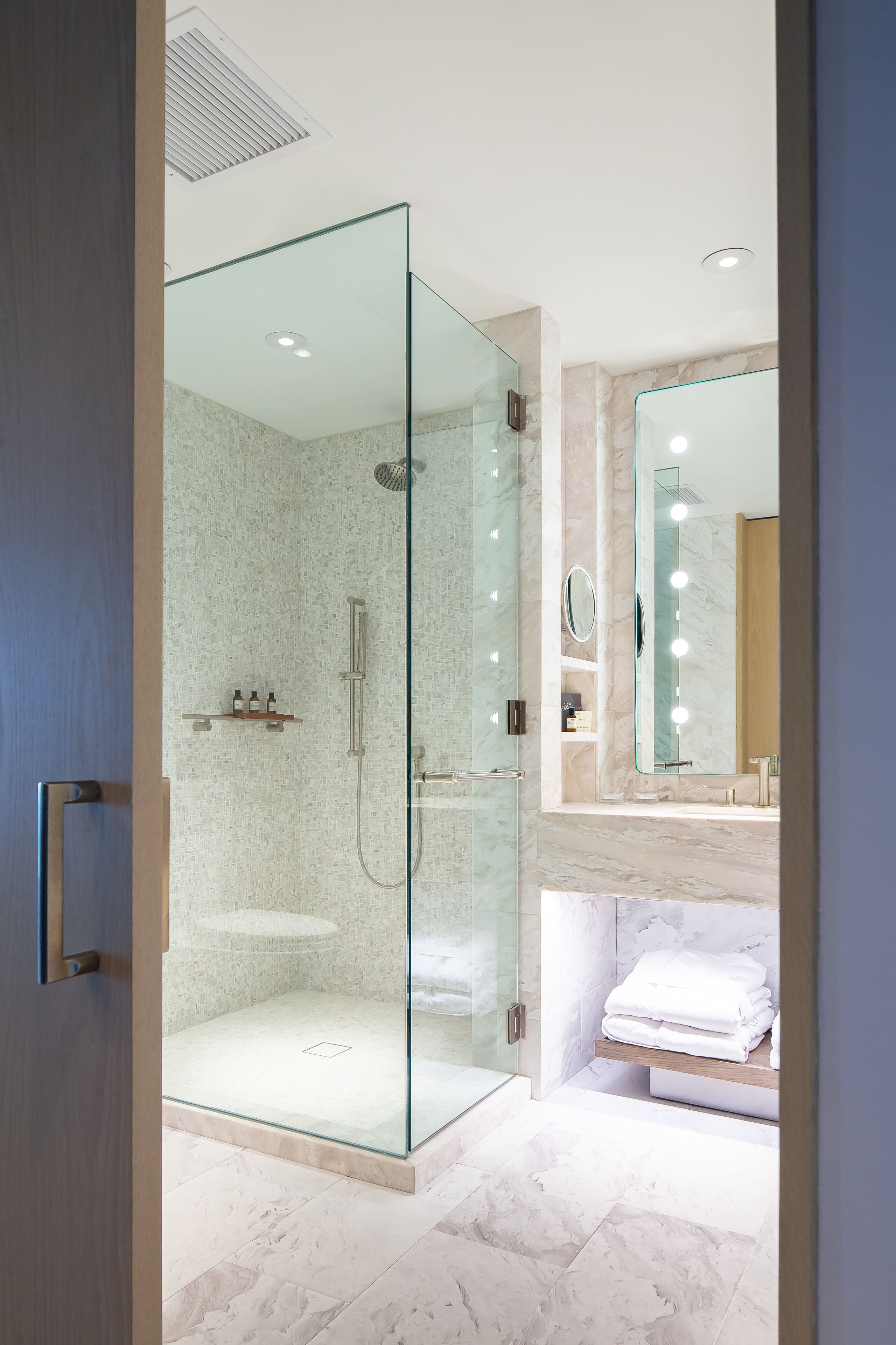 A modern bathroom with a glass-enclosed shower, a vanity with a mirror, and a marble floor.