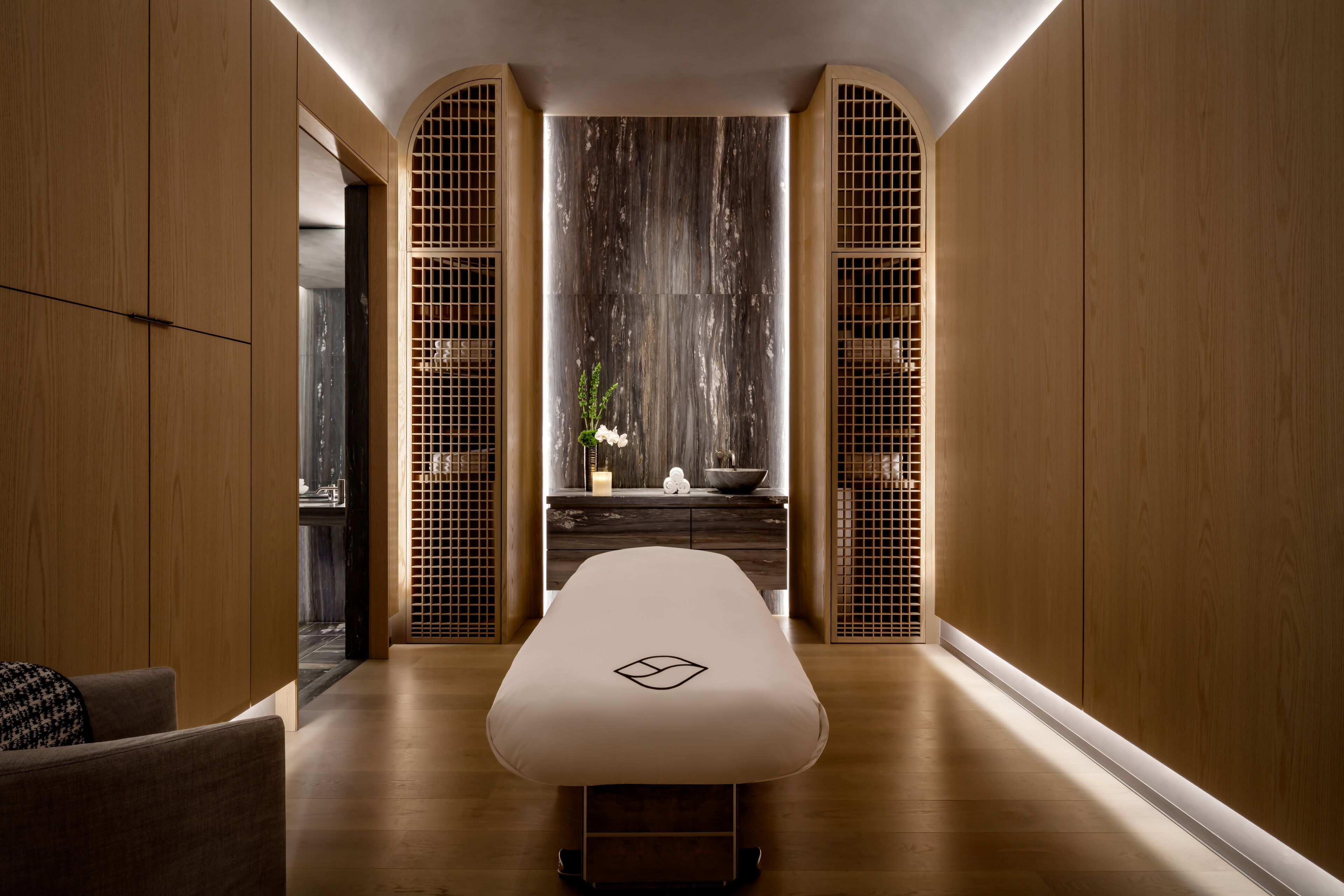 A modern spa room with a wooden floor, a massage table, and a wooden wall with a decorative screen.