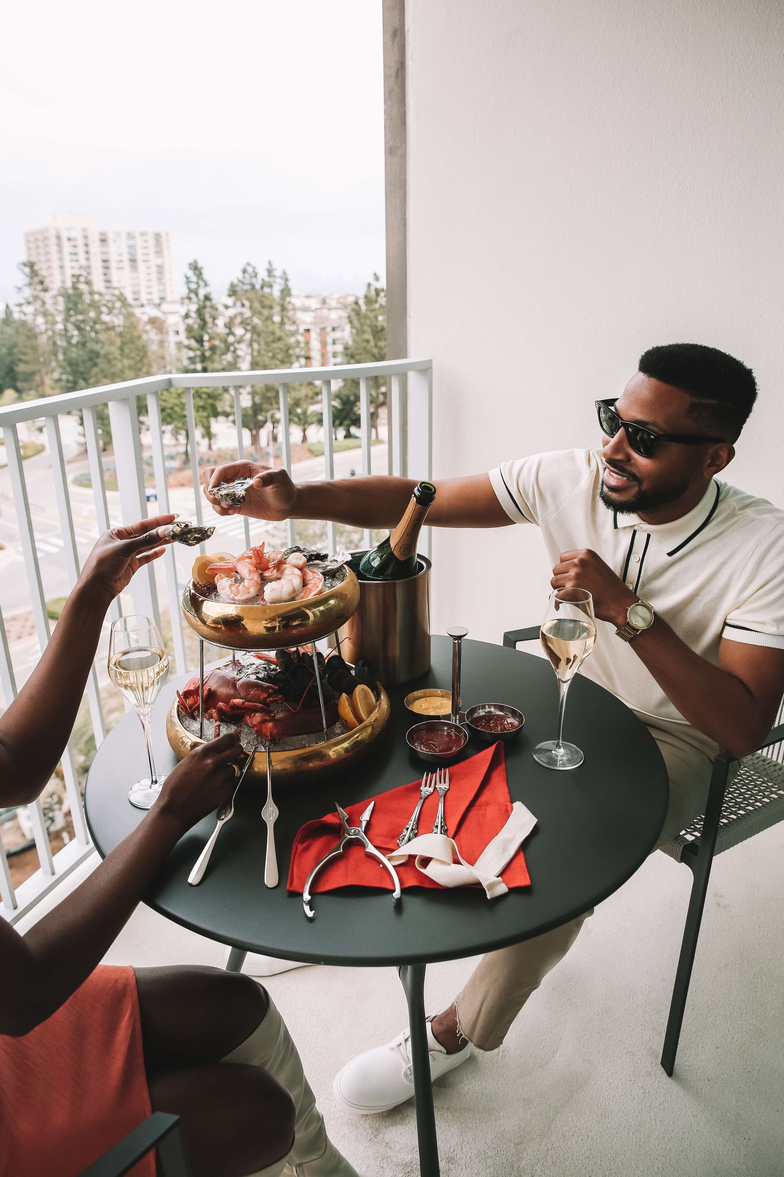 A balcony with a dining table set for two, featuring a seafood platter, wine glasses, and a bottle of champagne.