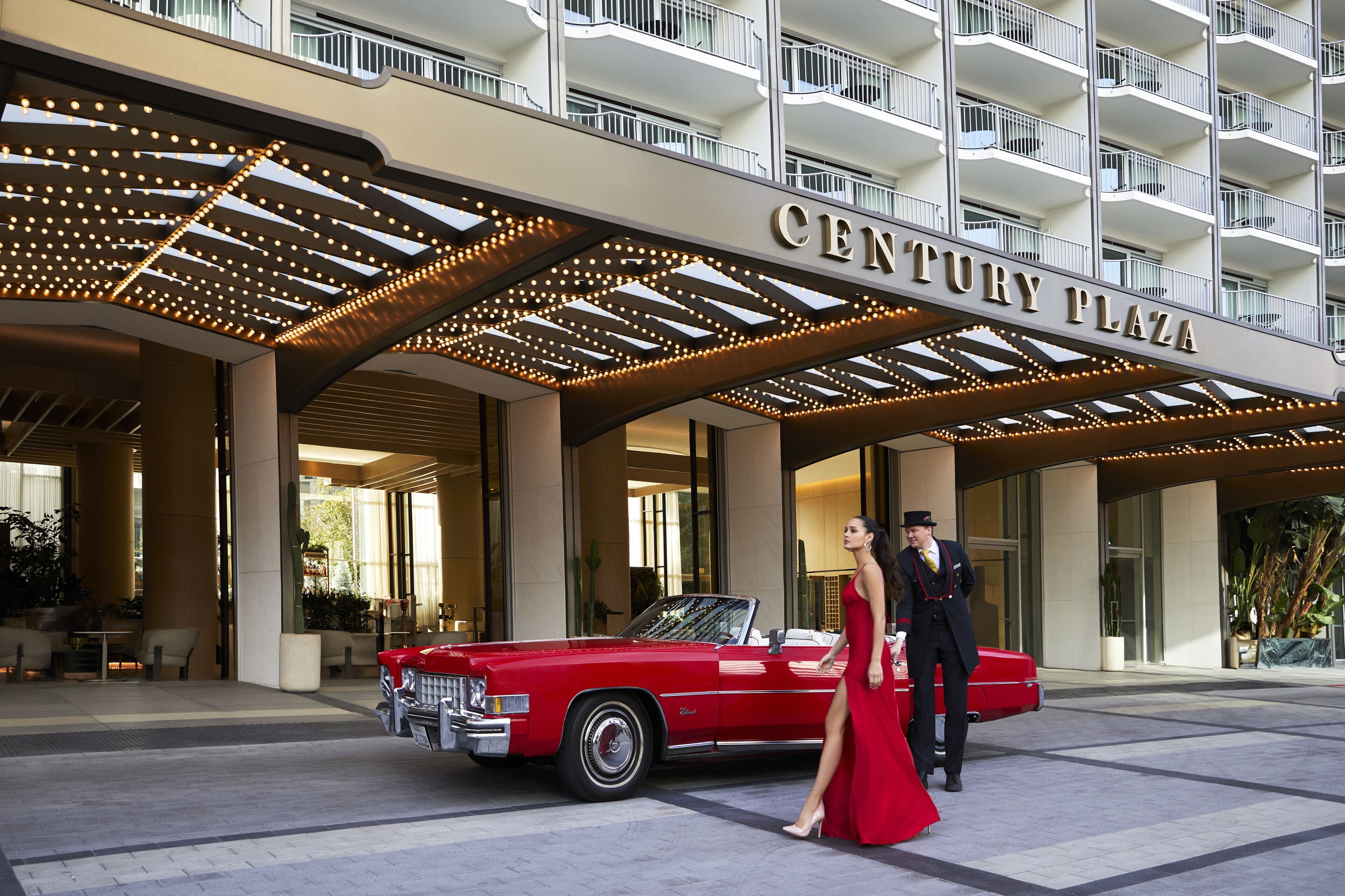 En röd, klassisk bil parkerad framför hotellet Century Plaza, med en man och en kvinna som bär formella kläder.