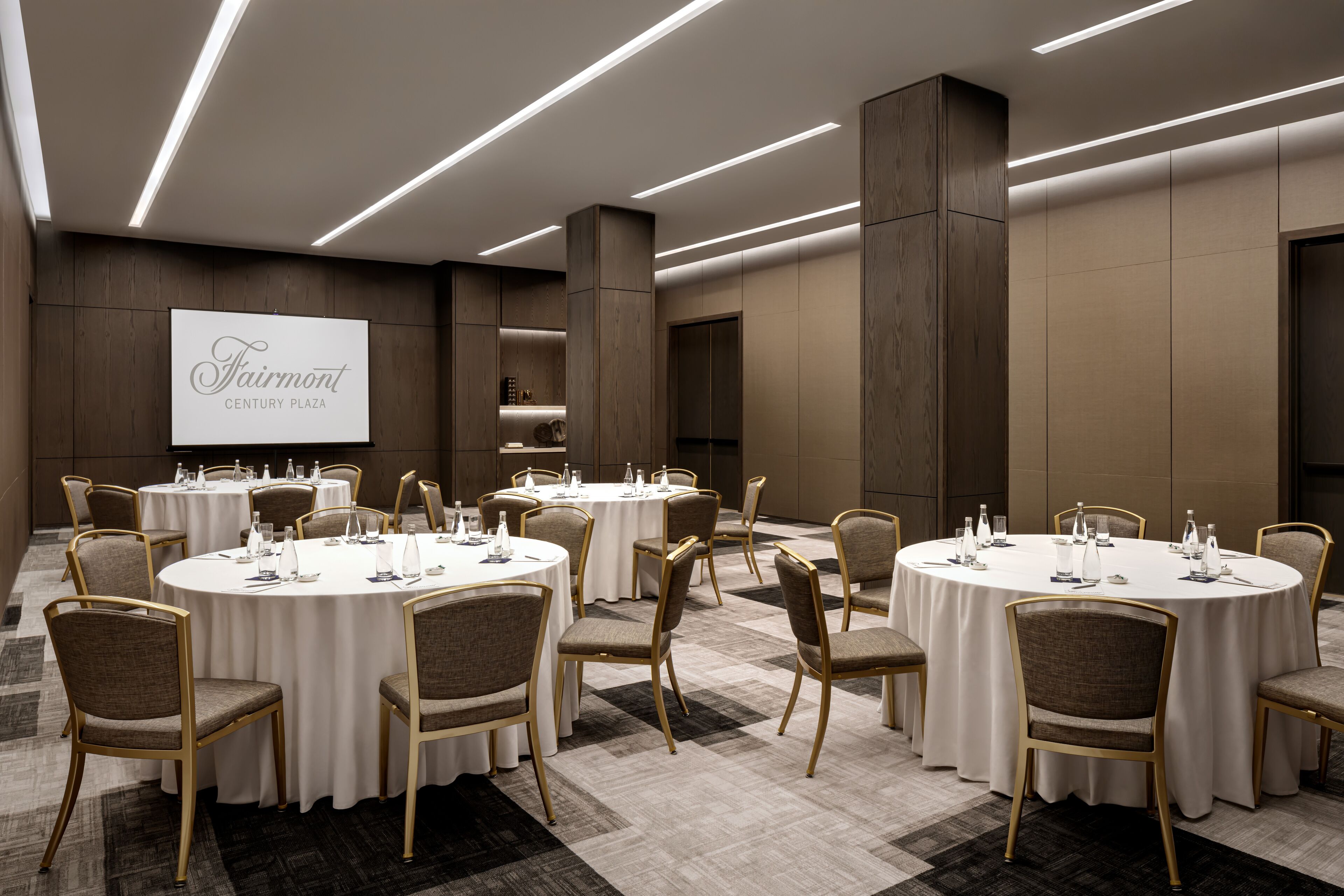 A conference room with round tables, chairs, and a projection screen displaying "Fairmont Century Plaza".