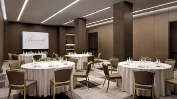 A conference room with round tables, chairs, and a projection screen displaying "Fairmont Century Plaza".