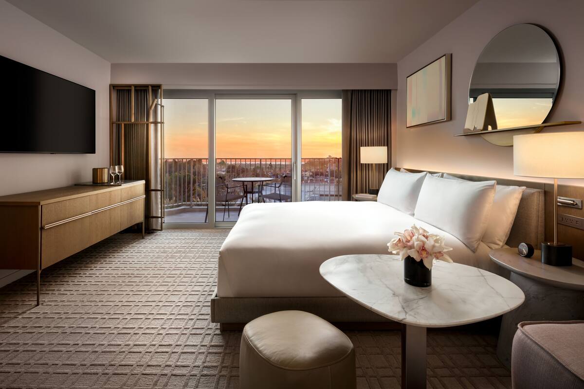 Ein modernes Hotelzimmer mit einem großen Bett, einem Flachbildfernseher, einem Esstisch und einem Balkon mit Blick auf die Stadt.