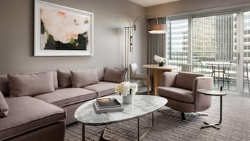 Un salon moderne avec un canapé d’angle, une table basse ronde et une petite table d’appoint. Un tableau abstrait encadré est accroché au mur, et une lampe sur pied est posée à proximité.