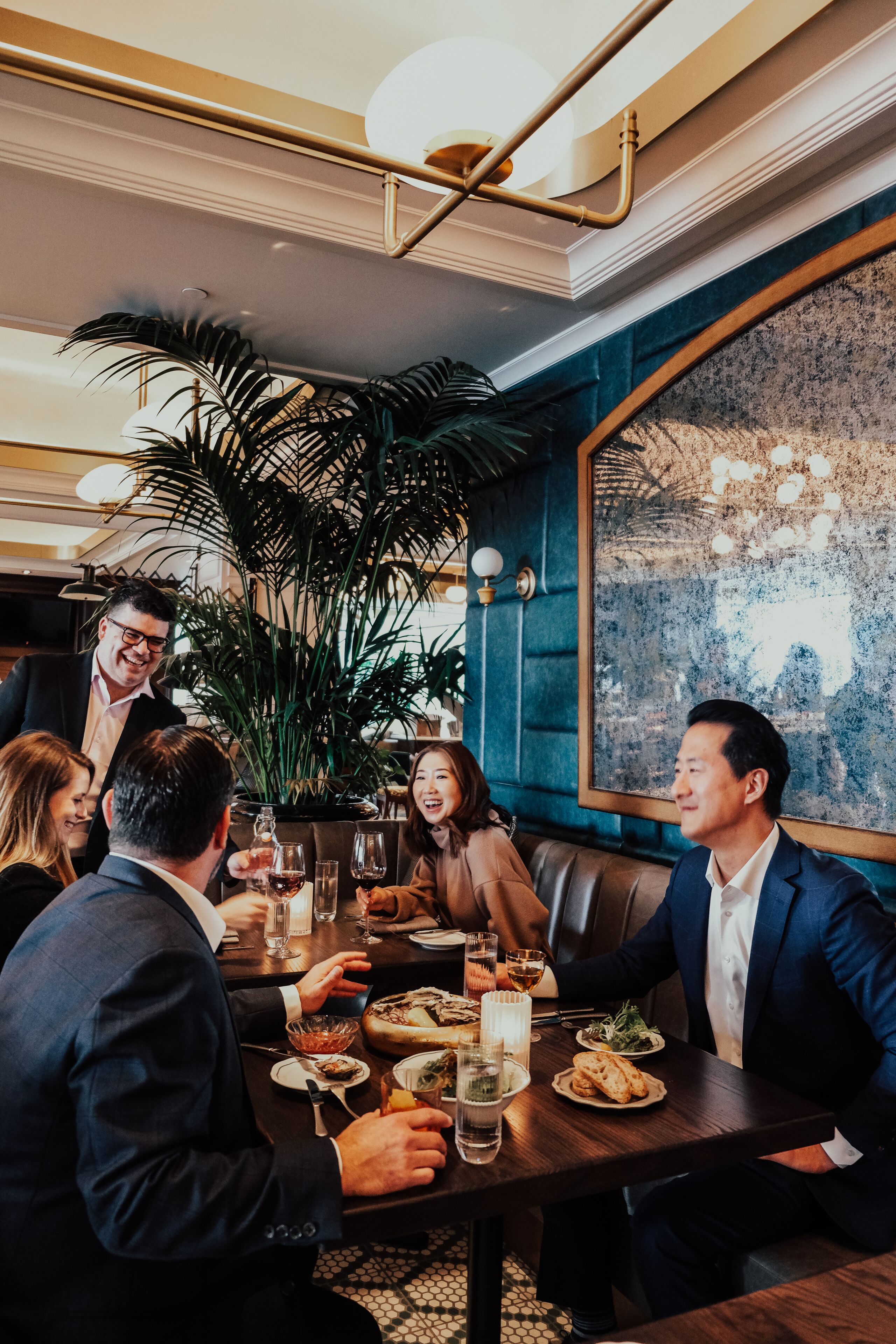 A group of people dining at a restaurant with a large plant and a cityscape view.