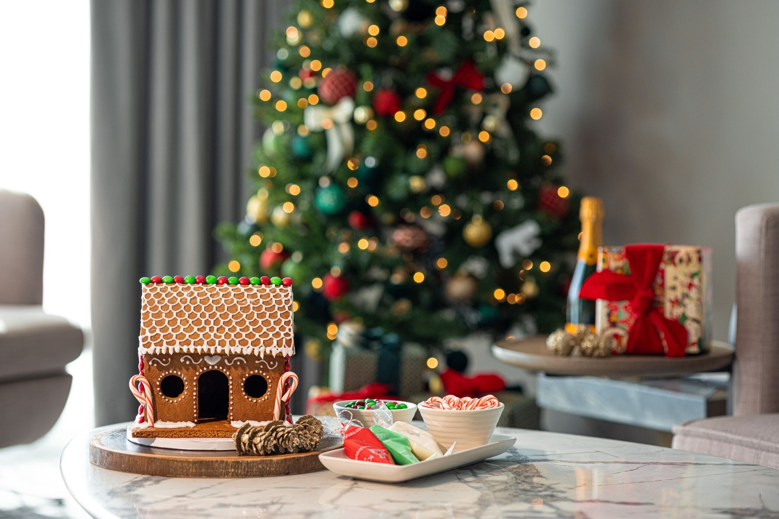 A gingerbread house on a table with a Christmas tree in the background.