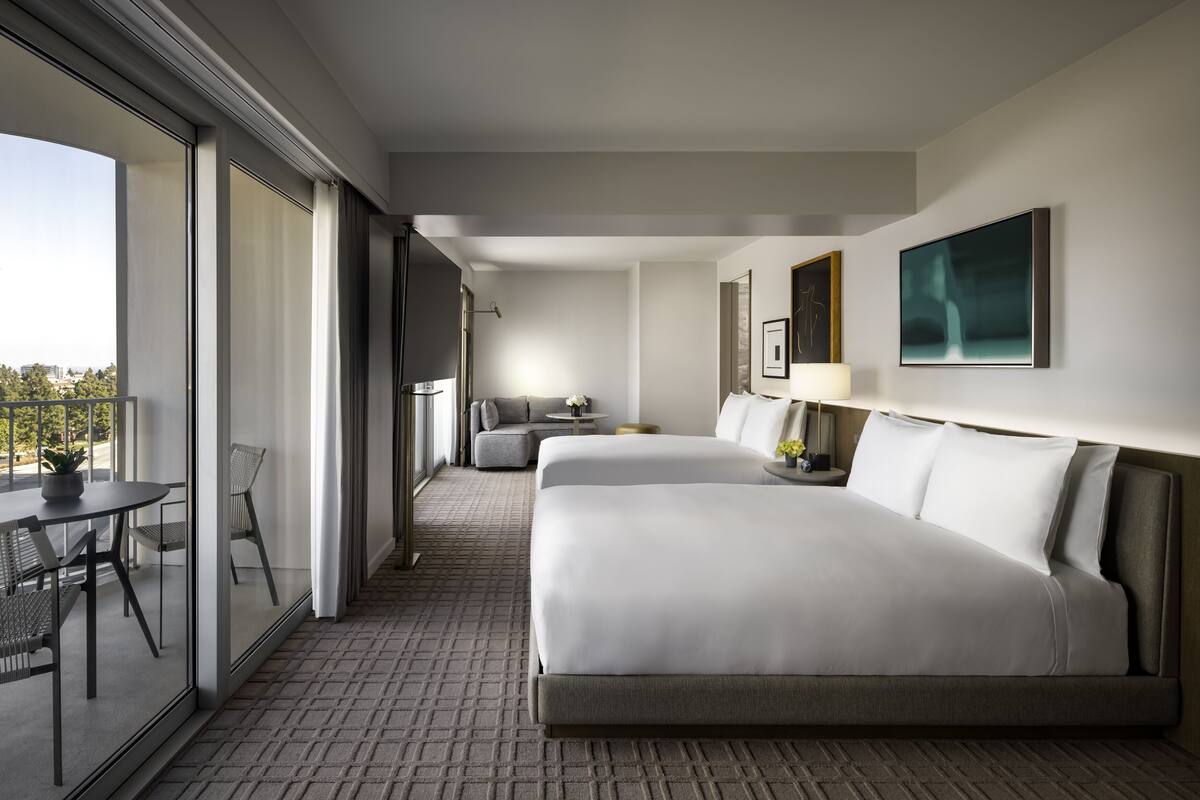 Ein modernes Hotelzimmer mit einem großen Bett, einer Sitzecke, einem Balkon mit Tisch und Stühlen und Blick auf die Stadt.