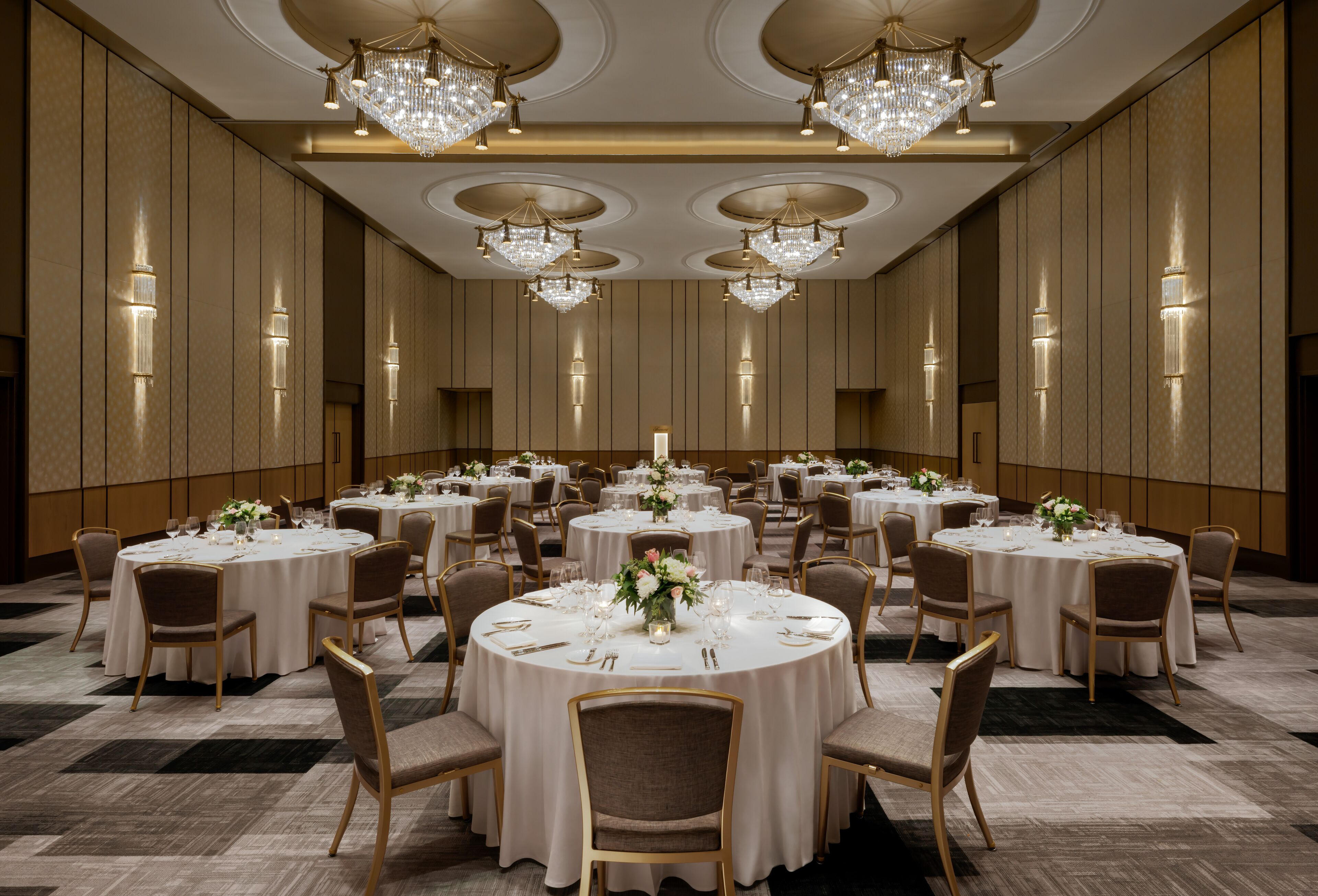 Une vaste salle de banquet avec des tables rondes, des lustres et des appliques murales.