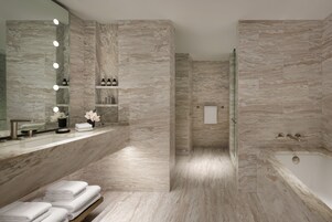 Un baño moderno con pared de mármol, cabina de ducha de vidrio, tocador con espejo y bañera.