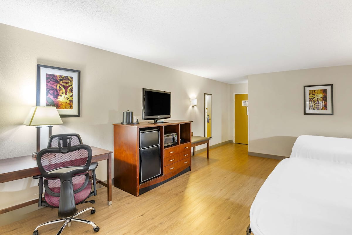 A hotel room with a bed, desk, chair, TV, and a minibar.