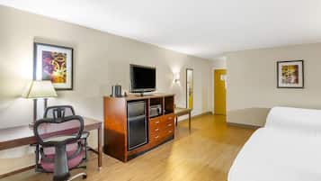 Camera d'albergo con letto, scrivania, sedia, televisore e un minibar.