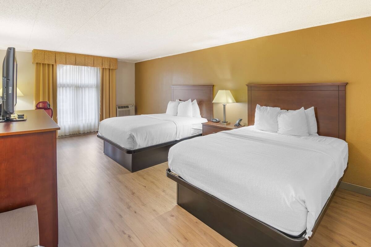 A hotel room with two beds, a desk, a TV, and a window with curtains.