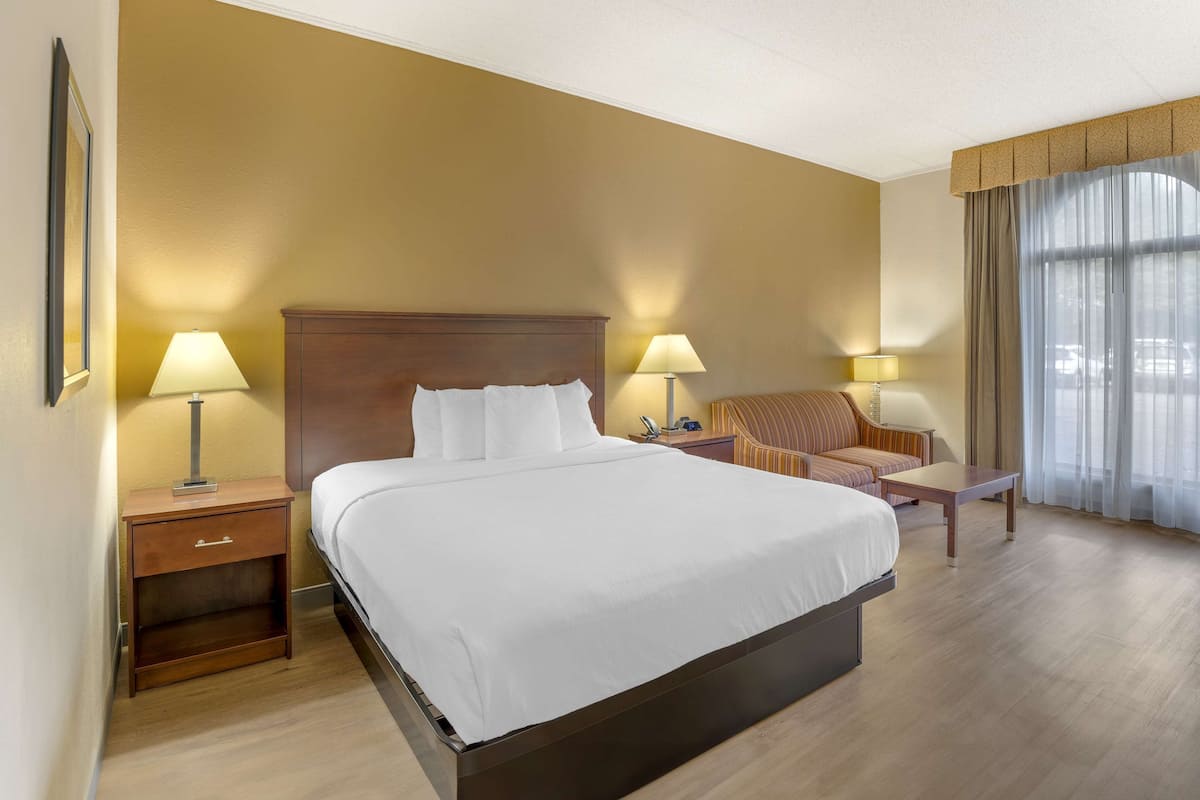 A hotel room with a large bed, two bedside tables with lamps, a chair, and a small table.