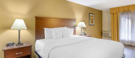 Habitación de hotel con una cama grande, dos mesitas de noche con lámparas, una mesita de madera, un teléfono en la pared y una ventana con cortinas.