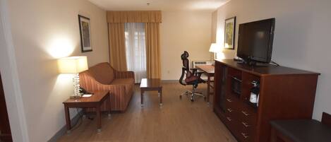 A hotel room with a sofa, a desk, a television, and a cabinet.