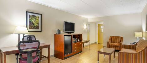 A hotel room with a desk, office chair, sofa, TV, and a small cabinet.