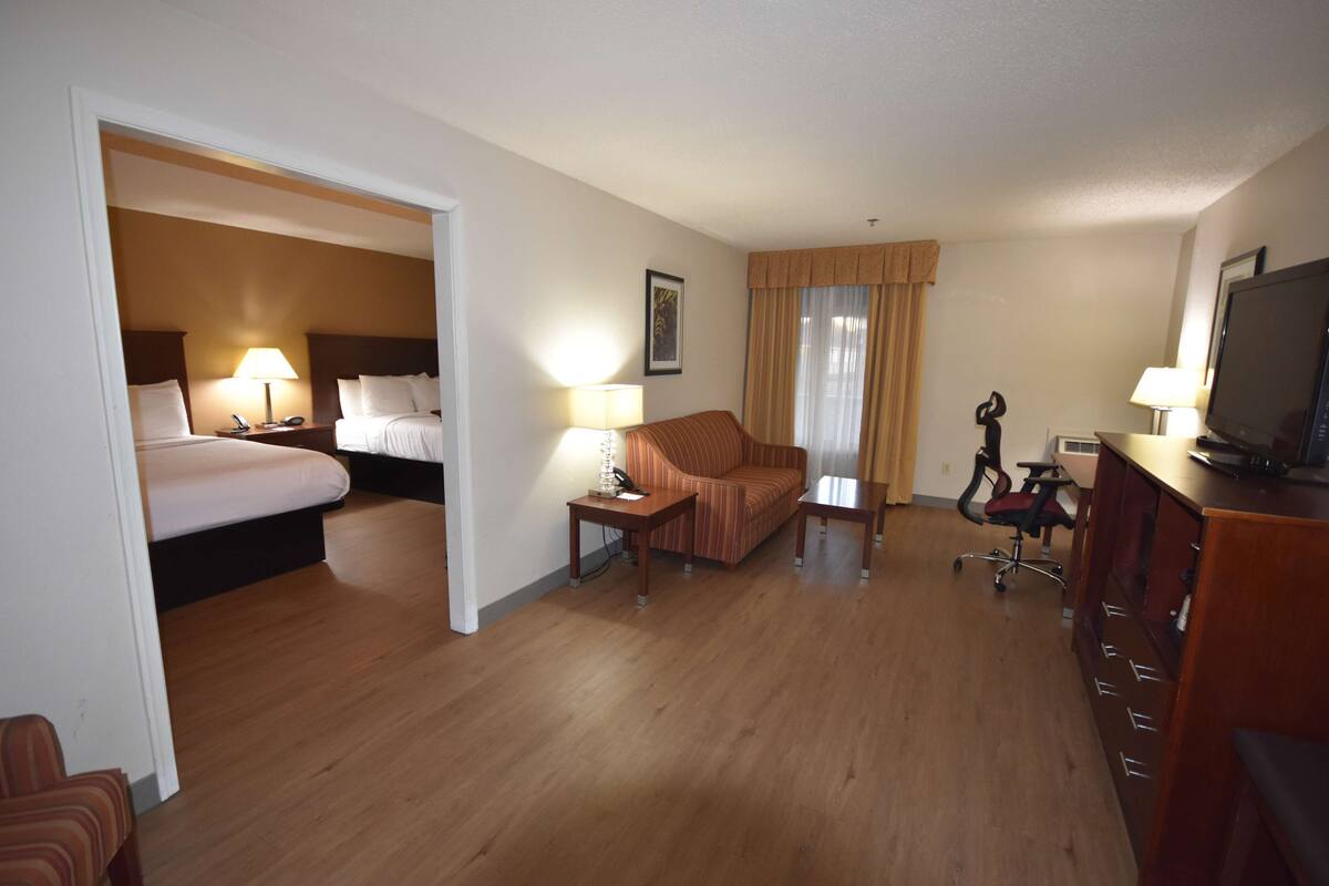 A hotel room with a bed, a sofa, a desk with a chair, a television, and a window with curtains.