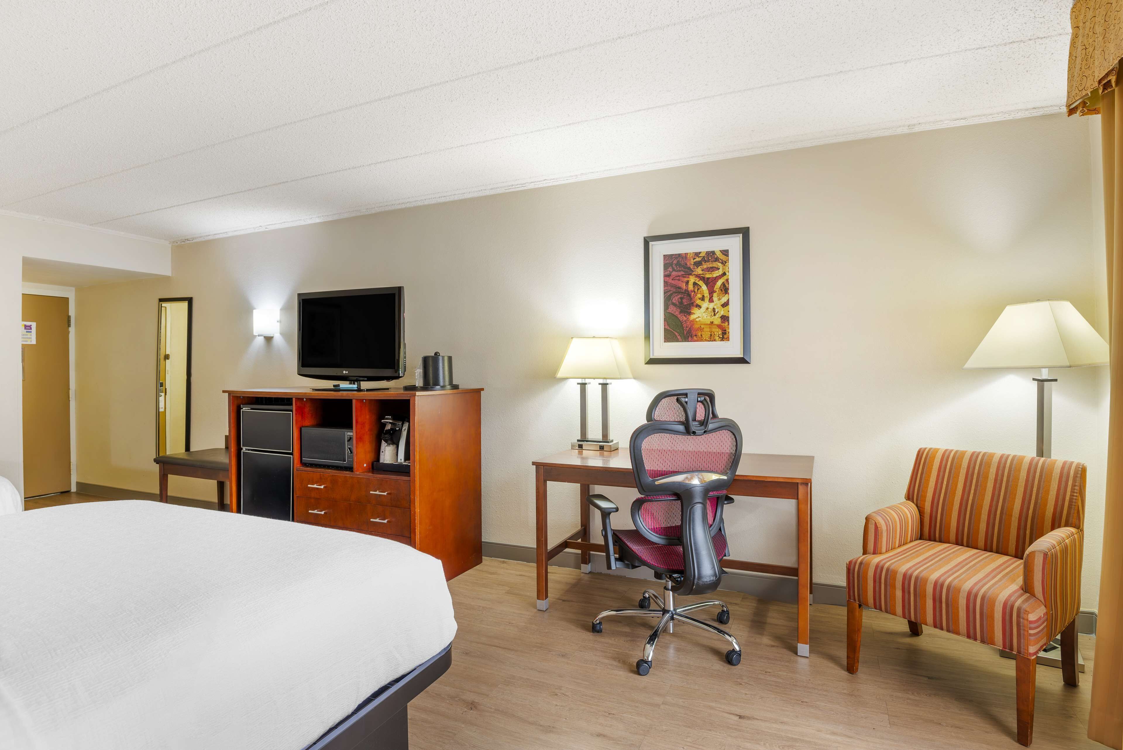 Habitación de hotel con cama, escritorio, silla, televisión y lámpara.