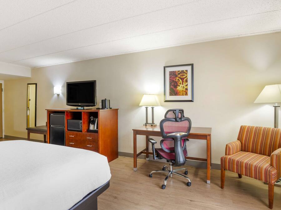 Habitación de hotel con cama, escritorio, silla, televisión y lámpara.