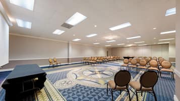 Un salón de conferencias con filas de sillas, un proyector y una alfombra estampada.