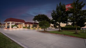 A Red Roof Inn with a red roof and brick facade, a parking lot, and a grassy area with trees. - Red Roof Inn & Conference Center McKinney (McKinney)