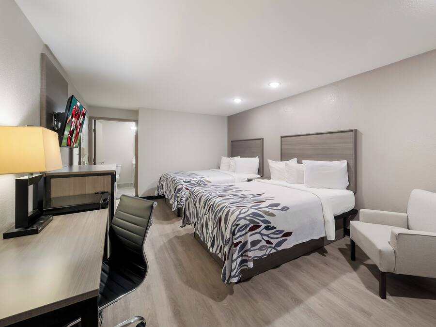 A hotel room with a bed, two bedside tables, a desk with a chair, a TV, and a lamp.