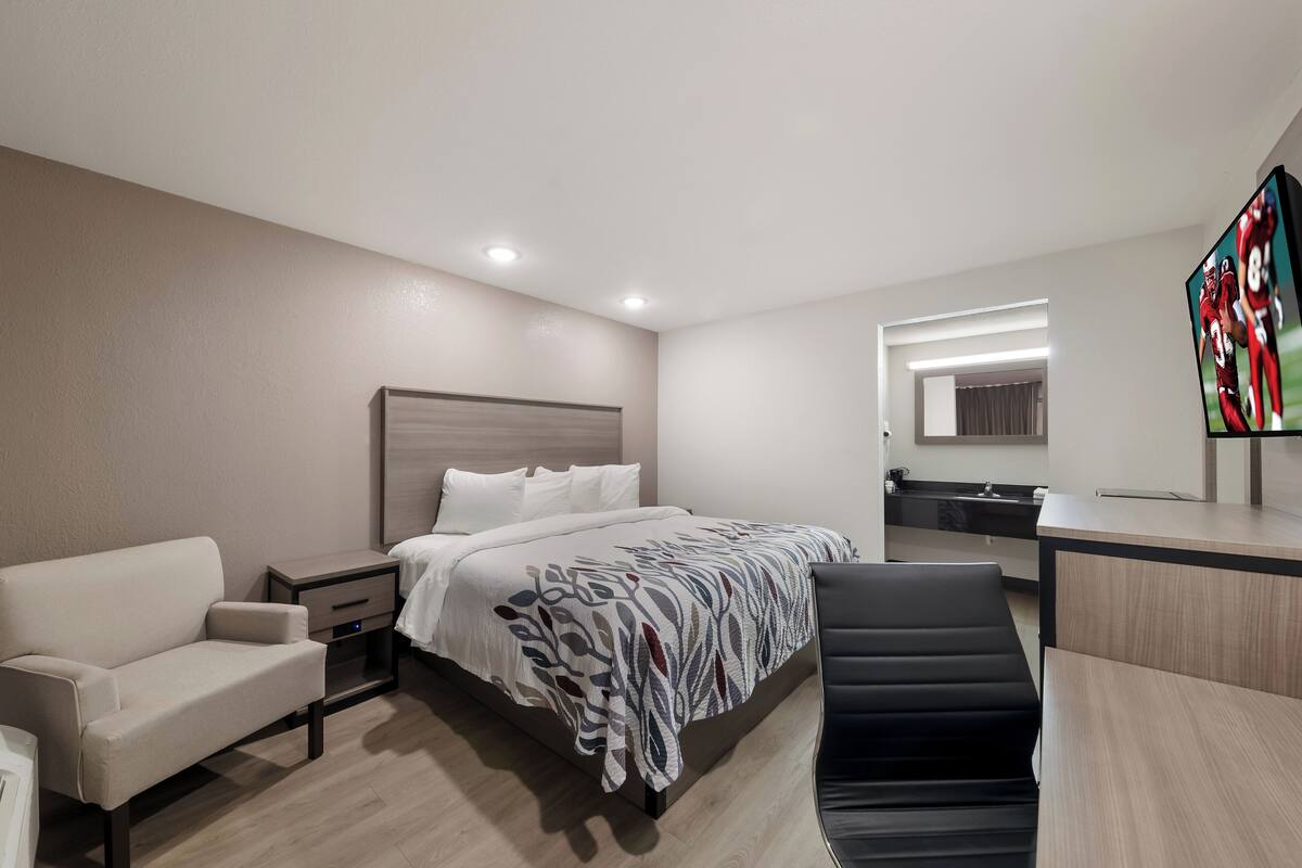 A modern hotel room with a bed, a desk, a chair, a sofa, and a TV.